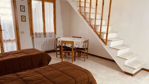 A bedroom with two beds, a wooden staircase, and a dining table with chairs.