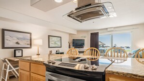 A modern kitchen with a central island, wooden chairs, a dining table, and a large window with a view. - Stunning views from this bayfront condo in the Taft district of Lincoln City! (Lincoln City)