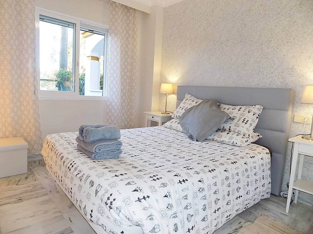 A bedroom with a bed, two bedside tables, a window, and a nightstand.