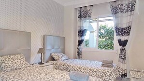 A hotel room with two beds, a large window with curtains, and a view of greenery outside.