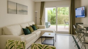 A modern living room with a sofa, coffee table, and chairs. There is a TV mounted on the wall and a sliding glass door leading to an outdoor area.