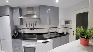 A modern kitchen with grey cabinets, a black countertop, a stainless steel range hood, a microwave, a dishwasher, and a potted plant.