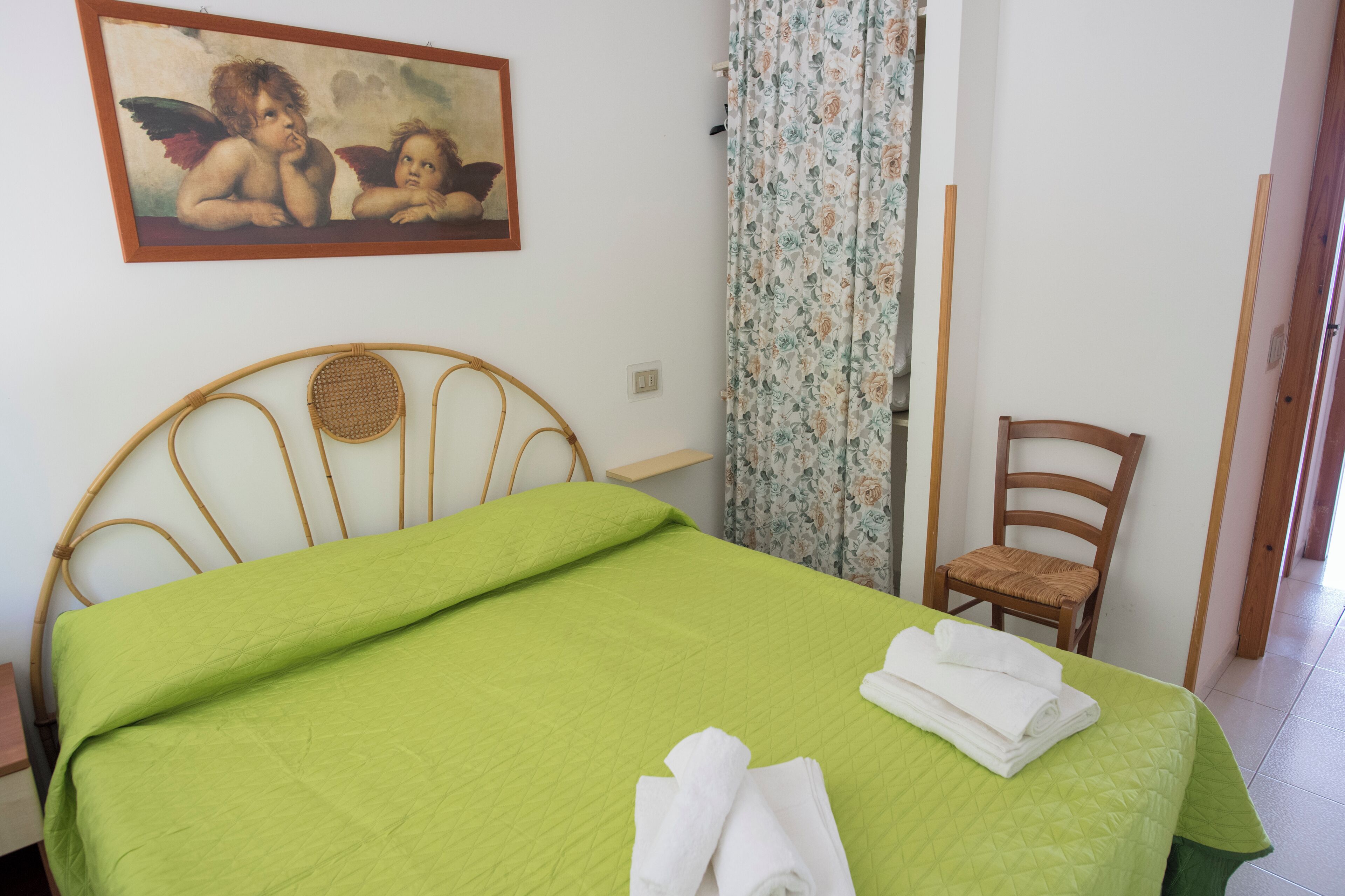 Una habitación con cama, una silla, un cuadro y una cortina.