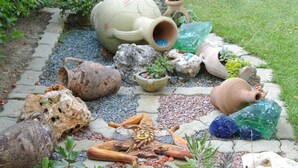 A garden with various decorative items including pottery, rocks, and plants.