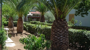 A garden with palm trees and a pathway leading to a building with a red roof.