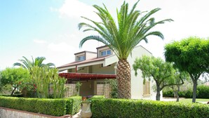 A two-story house with a red roof, surrounded by well-maintained hedges and palm trees.
