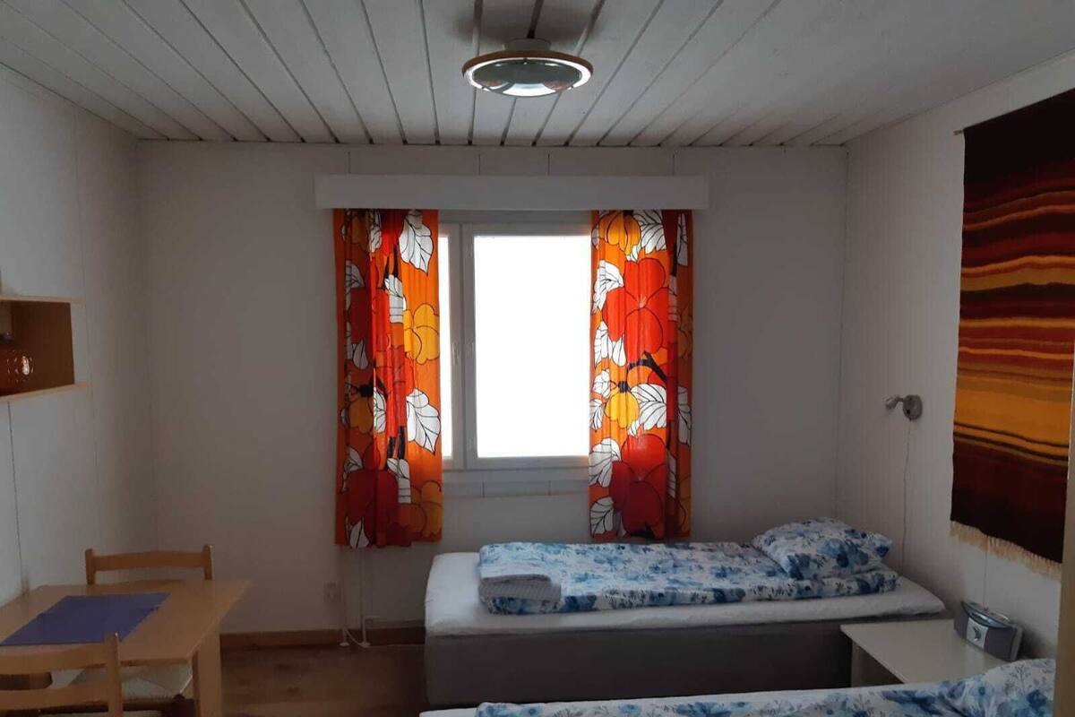 A small, simple room with two beds, a desk, and a window with curtains.