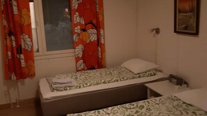 Un dormitorio con dos camas individuales, una ventana con persianas, un cuadro en la pared y una cortina con estampado floral.