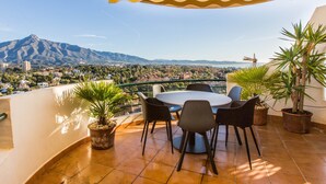 Eine Terrasse mit rundem Tisch und Stühlen, Topfpflanzen und Blick auf Berg und Stadtlandschaft.