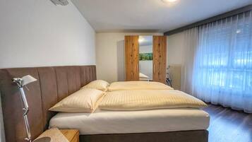 Una habitación de hotel con cama, lámpara de noche, cabecera de madera, ventana con cortinas y vistas a un bosque.