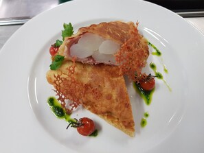 A plate with a slice of pie, garnished with parsley and a cherry tomato, and drizzled with green sauce. - Hotel Hecht (Rheineck)