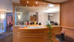 A reception area with a wooden reception desk, a glass partition, and a reception sign. - Hotel Hecht (Rheineck)
