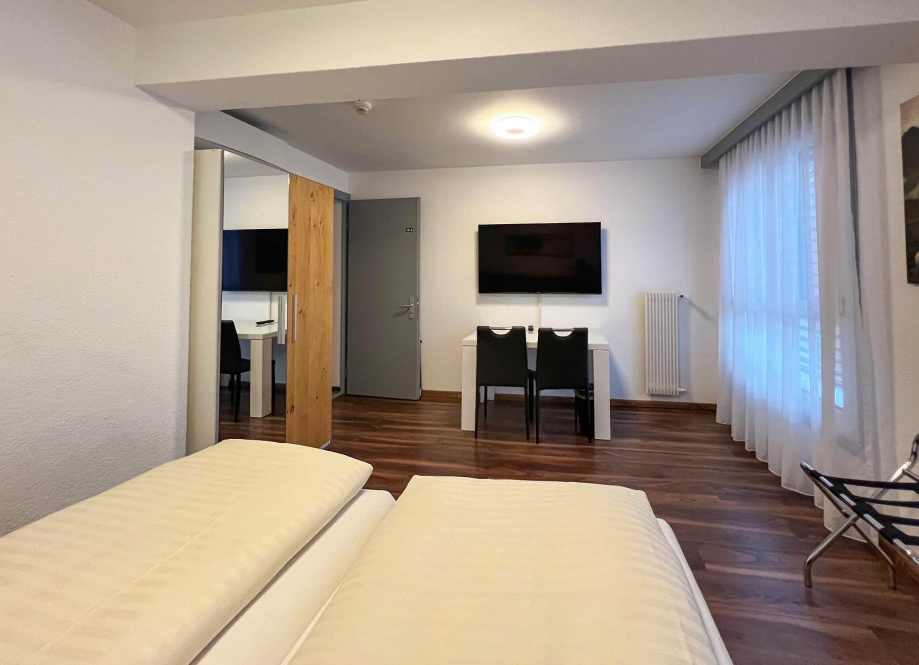 A hotel room with two beds, a TV, a desk, and a chair.