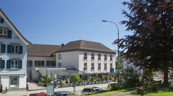 A hotel with a covered outdoor seating area, a parking sign, and a street view. - Hotel Hecht (Rheineck)