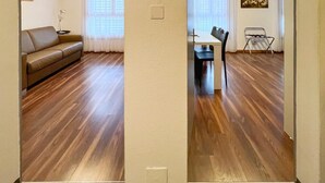 A room with a wooden floor, a sofa, a dining table with chairs, and a painting on the wall. - Hotel Hecht (Rheineck)