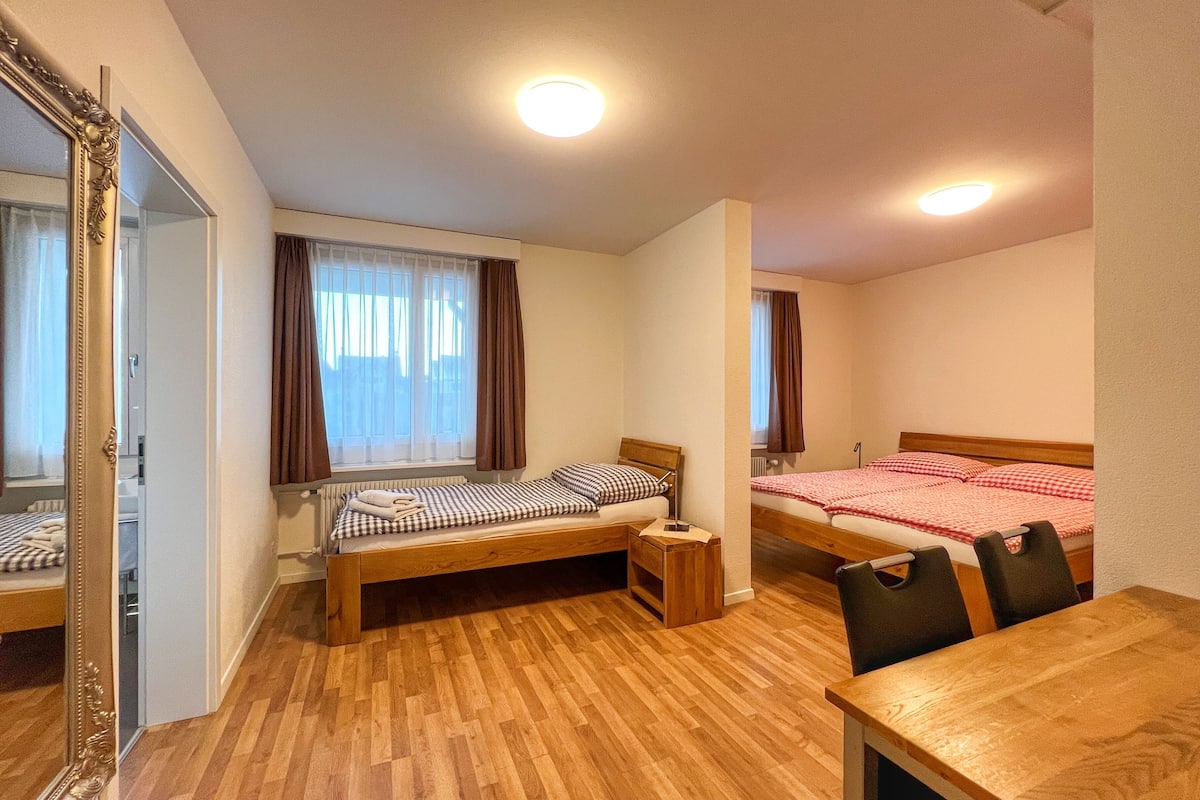 A hotel room with two single beds, a wooden floor, a wooden table, and a large mirror.