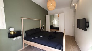 A modern bedroom with a wooden four-poster bed, a bedside table with a lamp, a mounted TV, and a mirror on the wall. - Design 2 Bdr Apartment - Habima TL60 (Tel Aviv)