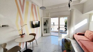 En moderne stue med sofa, spisebord med stole, tv ophængt på væggen og en skydedør til en udendørs balkon.