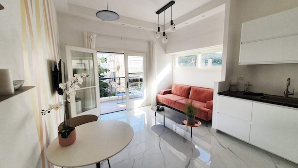 A modern kitchen with white cabinets, a red sofa, and a dining area with a table and chairs. - Design 2 Bdr Apartment - Habima TL60 (Tel Aviv)