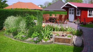 A well-maintained garden with a wooden table and chairs, a small pond, and a variety of plants.