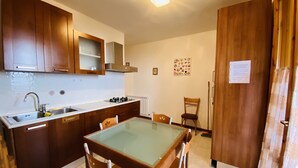 A compact kitchen with wooden cabinets, a stainless steel sink, and a glass-top dining table with four chairs. - Residence Le Terrazze sul Montefeltro (Carpegna)