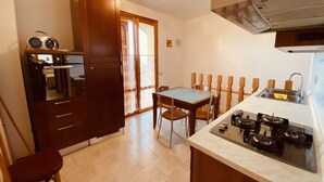 A compact kitchen with a dining area, a built-in oven, a gas stove, and a window with curtains. - Residence Le Terrazze sul Montefeltro (Carpegna)