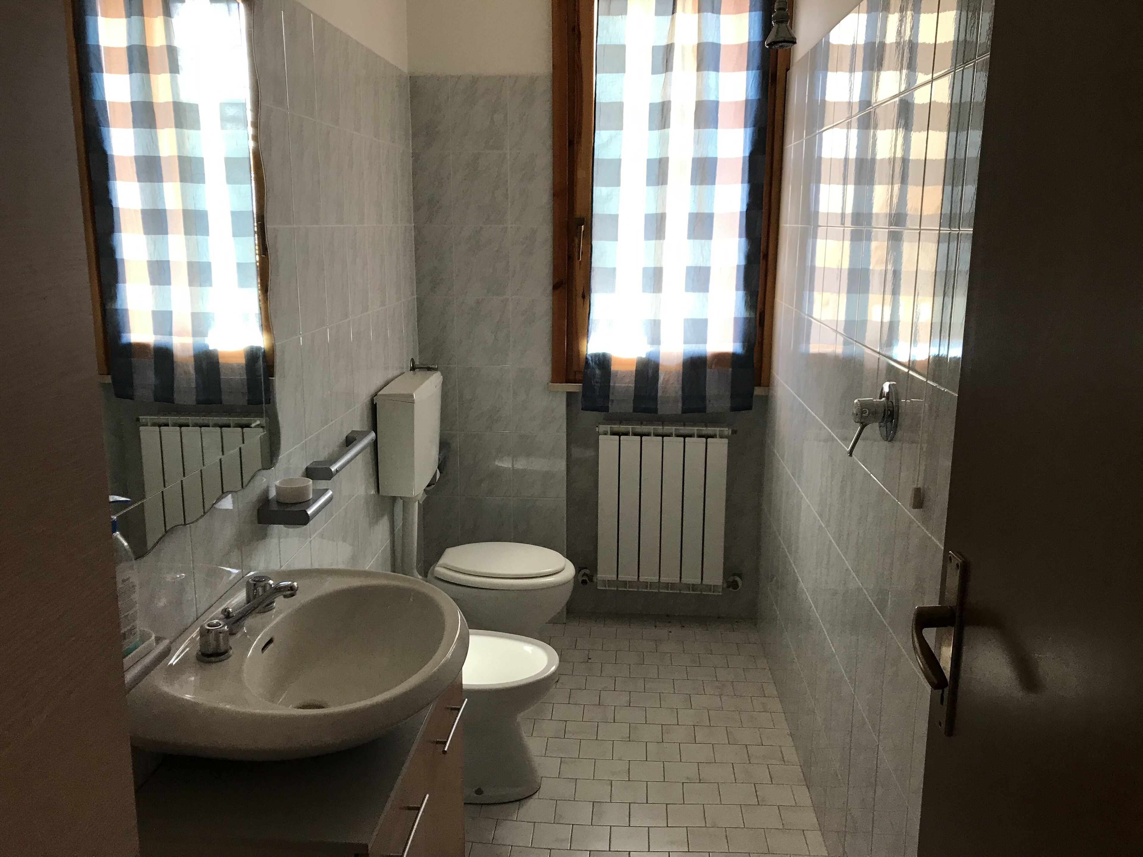 Un baño con lavamanos, inodoro y ventana con cortinas.