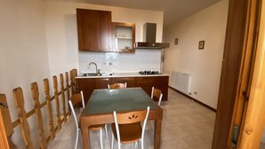 A compact kitchen with wooden cabinets, a gas stove, and a sink. There is a dining table with chairs. - Residence Le Terrazze sul Montefeltro (Carpegna)