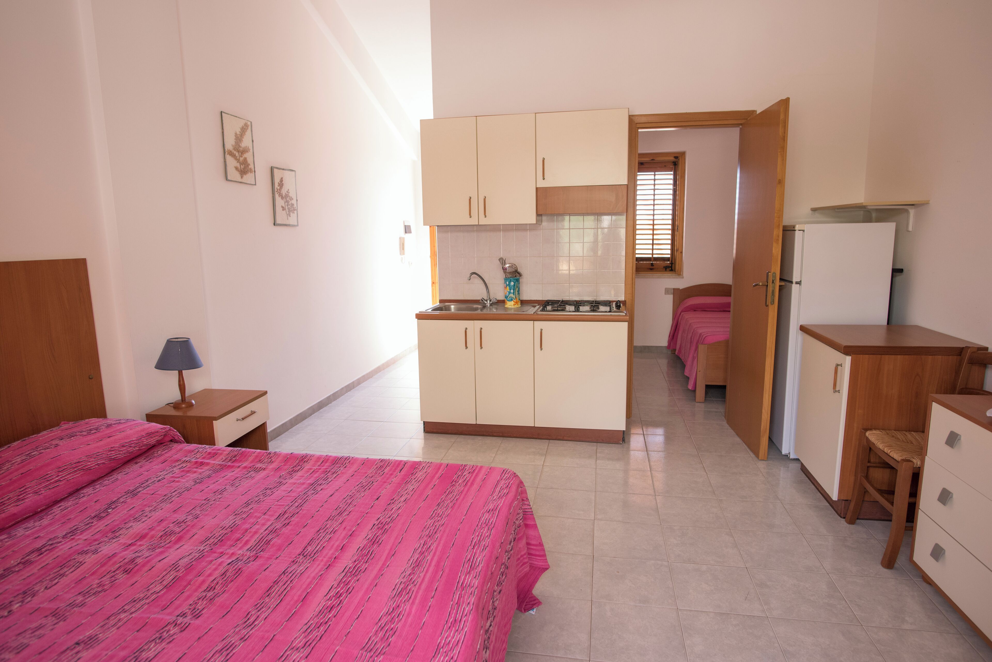 Un dormitorio con cama, mesita de noche, escritorio, silla, kitchenette y baño.