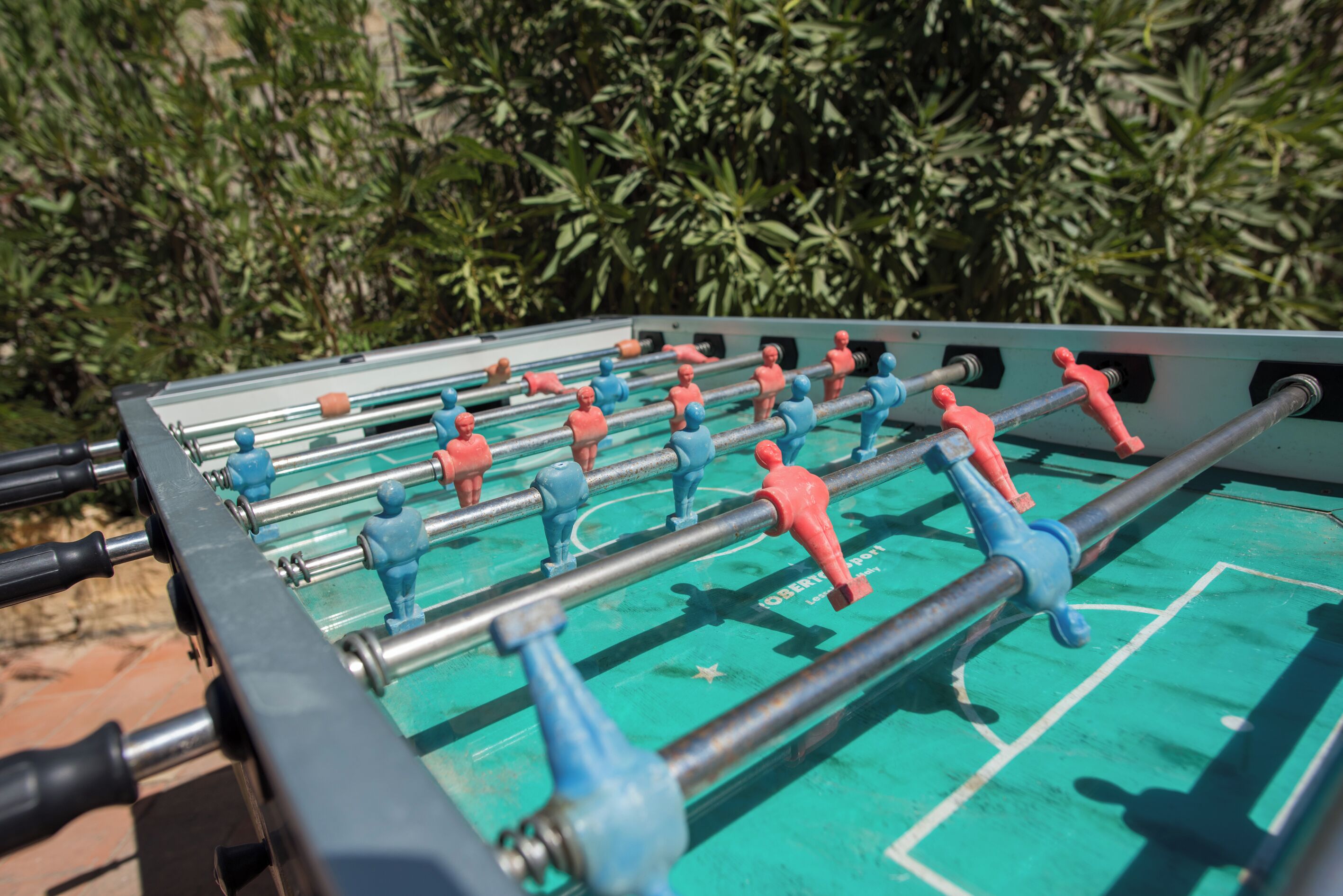Una mesa de fútbol de mesa con varios jugadores, frente a un fondo de follaje verde.