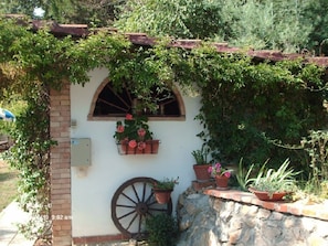 Un bâtiment rustique avec un mur en pierre, une roue en bois et des plantes en pot.