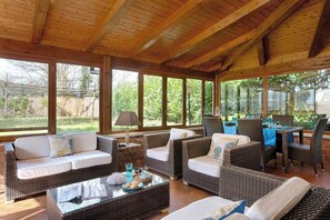 A covered outdoor seating area with wicker furniture, a dining table, and large windows. - Luxury Villa In Sorrento Coast Strategic Location (Massa Lubrense)