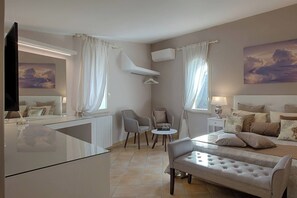 Ein modernes Schlafzimmer mit Bett, Nachttischen, Fernseher und einer Sitzecke mit Sesseln und einem Tisch.