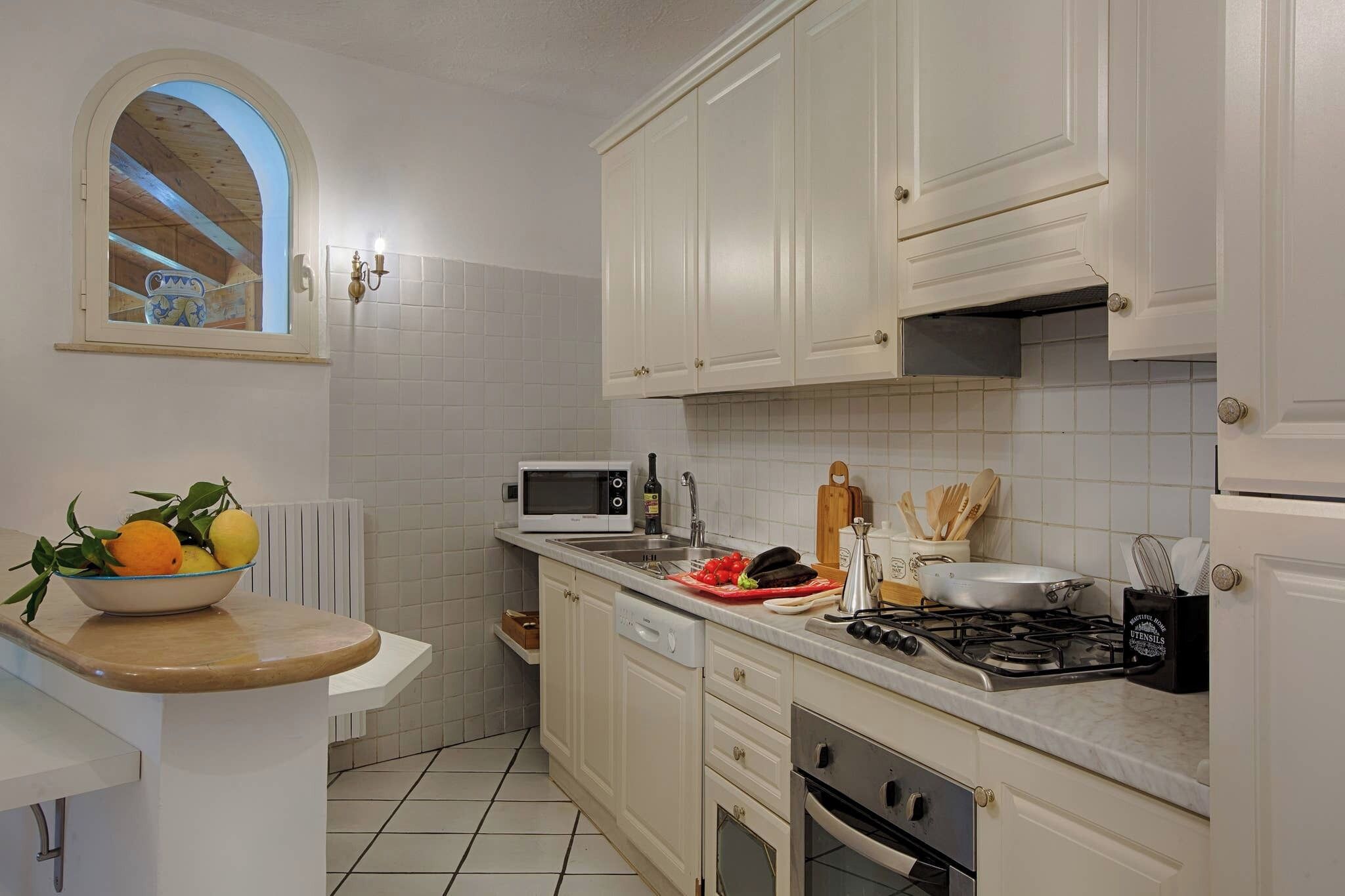 A kitchen with white cabinets, a microwave, a gas stove, and a bowl of fruit on the counter.