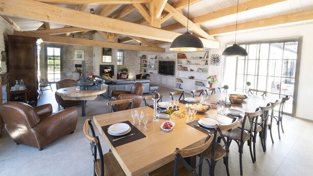Un vaste espace dédié à la salle à manger, avec une table en bois dressée pour le repas, entourée de fauteuils en cuir.