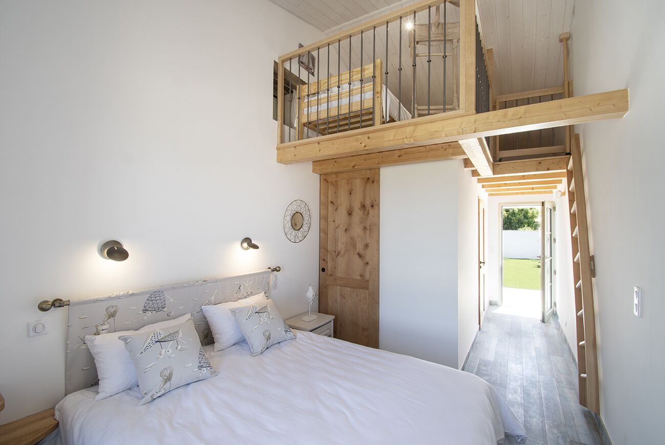 Une chambre à coucher comprenant un lit, des tables de chevet, une tête de lit en bois, un banc intégré et un espace de couchage en mezzanine.