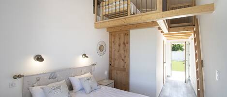 Une chambre à coucher comprenant un lit, des tables de chevet, une tête de lit en bois, un banc intégré et un espace de couchage en mezzanine.