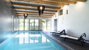Une piscine intérieure avec des parois en verre transparent, des poutres en bois et des chaises longues.