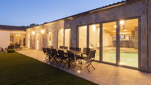 Une terrasse extérieure avec une table et des chaises, une piscine et un bâtiment en pierre doté de grandes fenêtres.