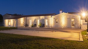 Un bâtiment en pierre doté de nombreuses portes et fenêtres, une allée pavée et un espace extérieur aménagé pour s’asseoir.