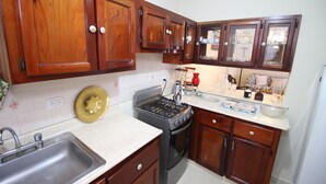 Una cocina con armarios de madera, un lavamanos de acero inoxidable, una estufa a gas y una encimera con distintos utensilios de cocina.