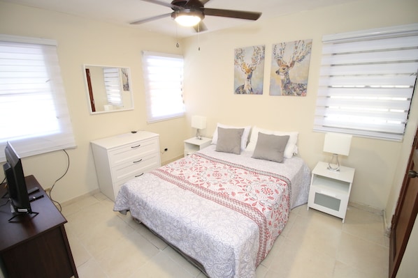 A bedroom with a bed, nightstands, a desk, and a ceiling fan.