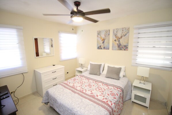 A bedroom with a bed, bedside tables, a ceiling fan, and artwork on the walls. - Hostal Caribean Apart (Santo Domingo)