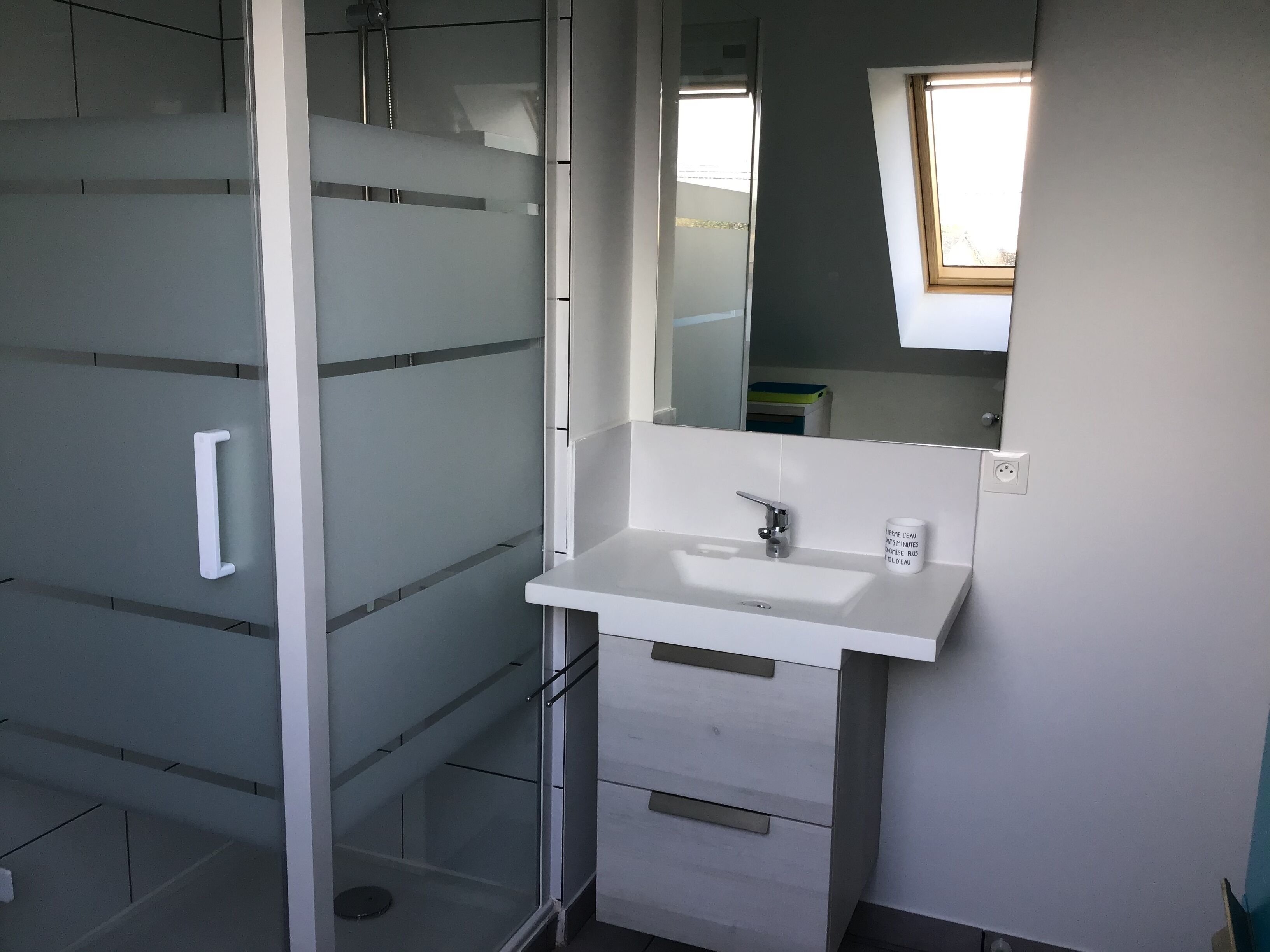 Un baño con cabina de ducha de vidrio, un lavabo blanco y un espejo sobre él.
