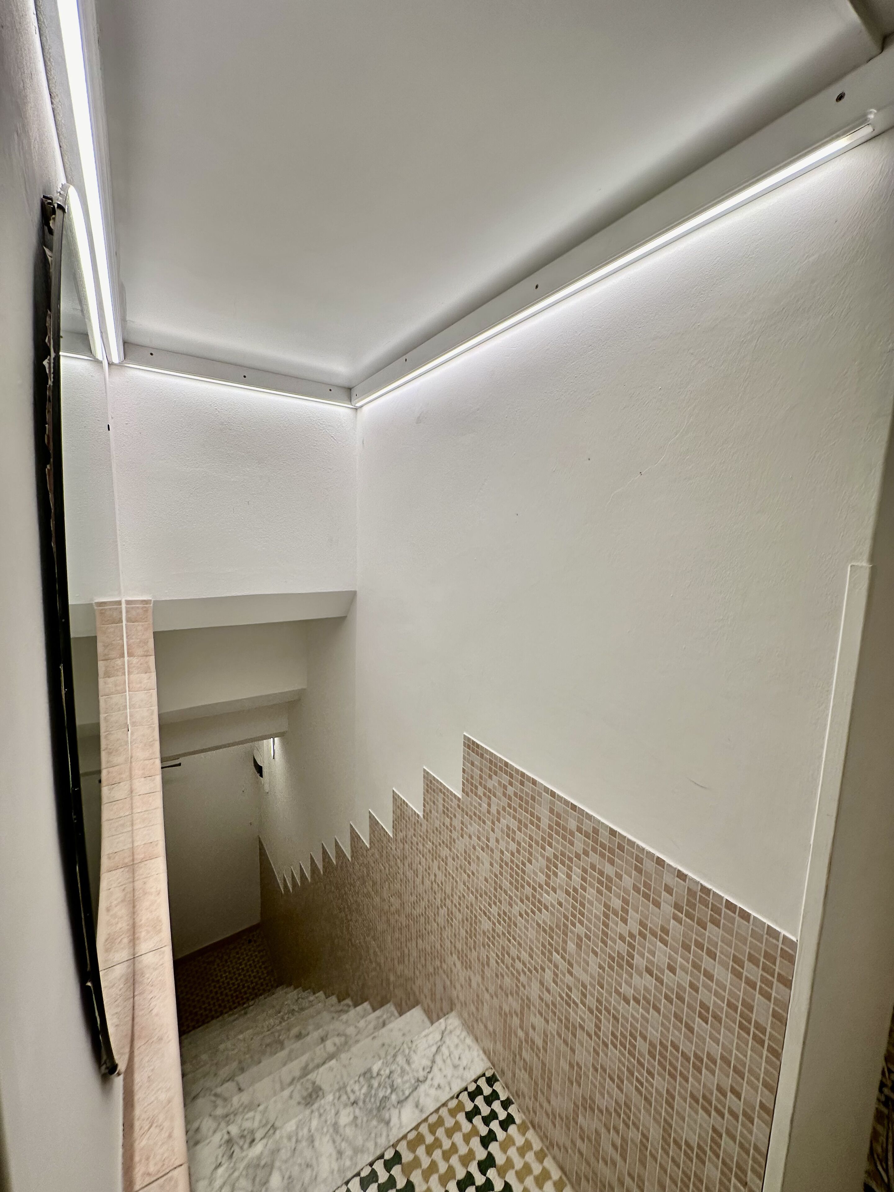 A narrow stairway with a tiled wall and a marble floor.