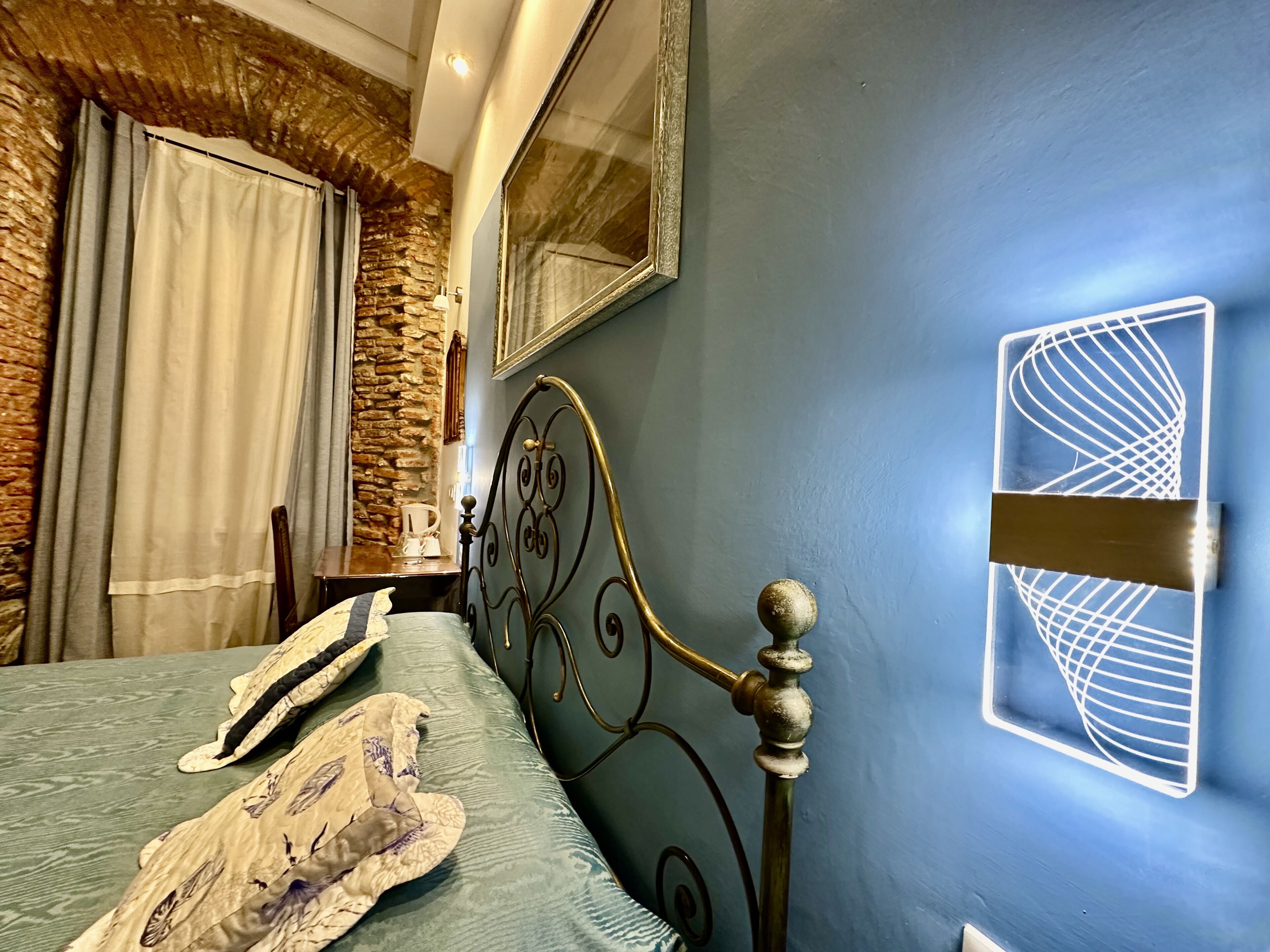 A bedroom with a bed, a stone wall, a mirror, and a unique wall light fixture.