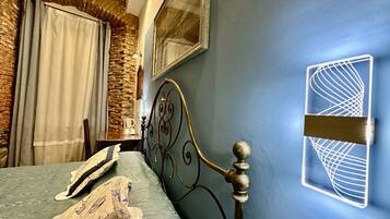 A bedroom with a bed, a stone wall, a mirror, and a unique wall light fixture.