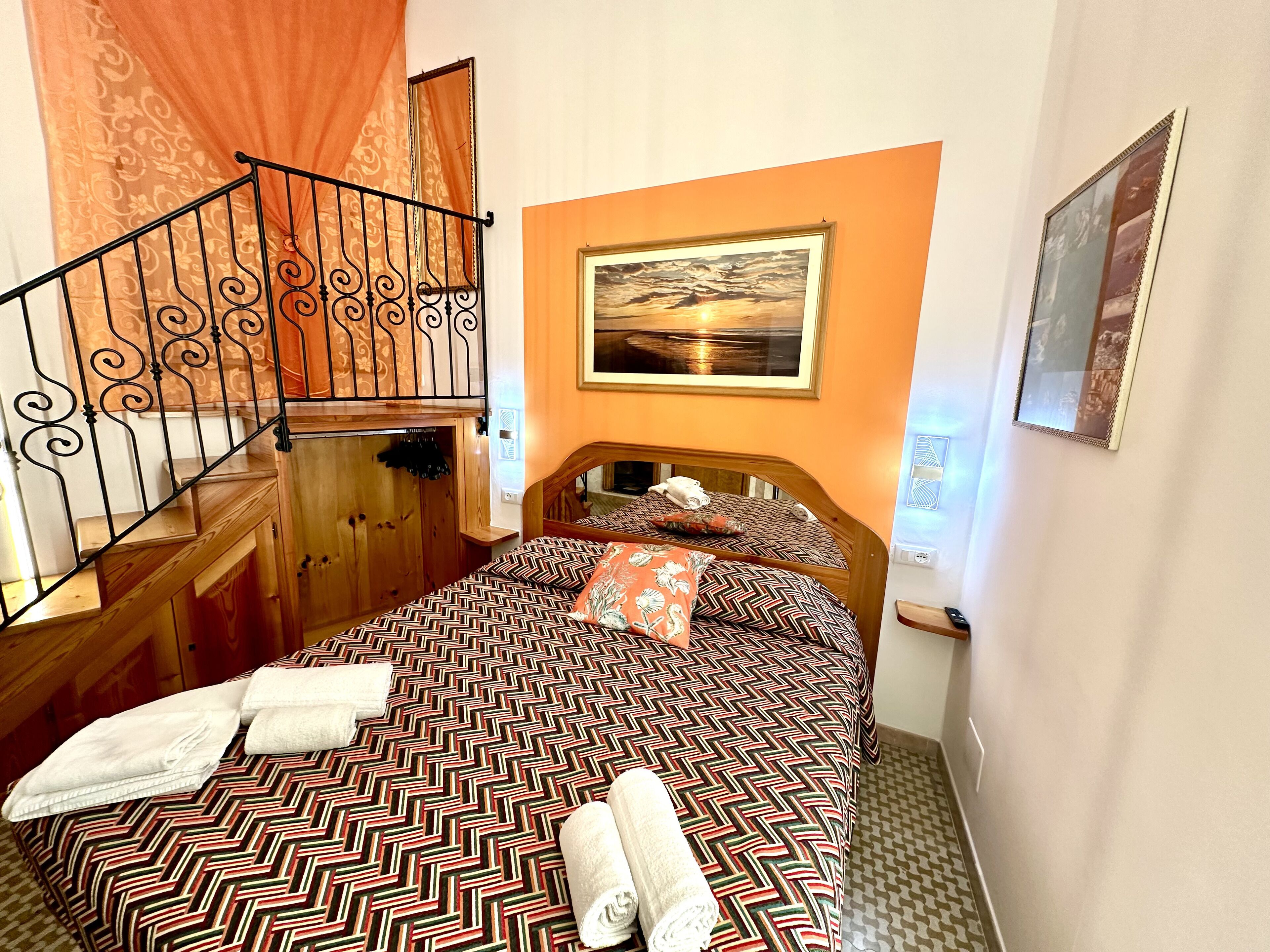 Una habitación de hotel con una cama, una escalera de madera, un cuadro en la pared y un espejo.