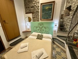 Un dormitorio con pared de piedra, cama con ropa de cama blanca, cabecera verde y una pintura de paisaje marino.