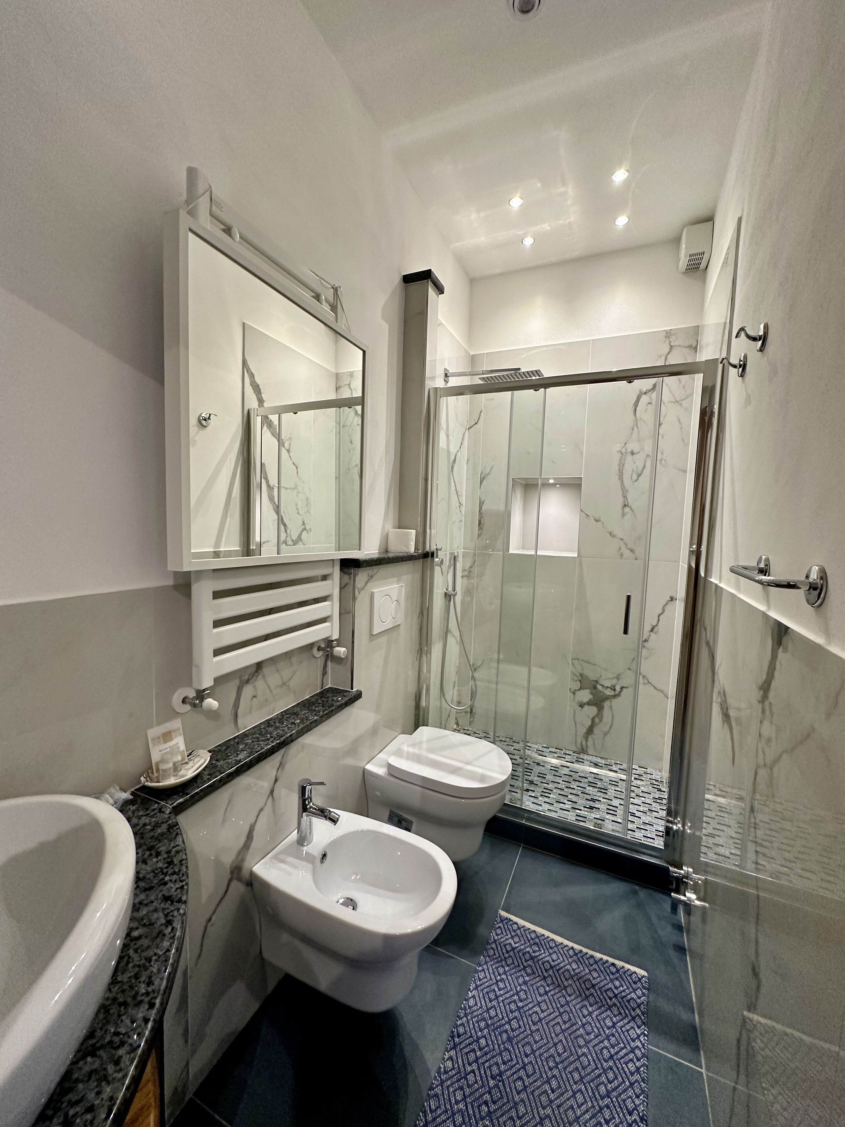 Un baño moderno con tocador de mármol, inodoro separado, ducha con cerramiento de vidrio y lavamanos empotrado.